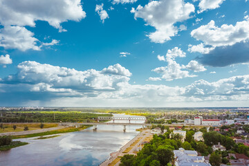Cityscape with a bridge over the river a bright day with a blue sky and clouds over the city. Many green areas and forests. Aerial view