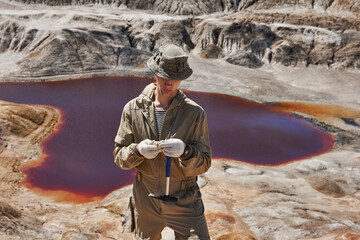 geologist examines a sample of mineral in the desert against the background of a salt lake