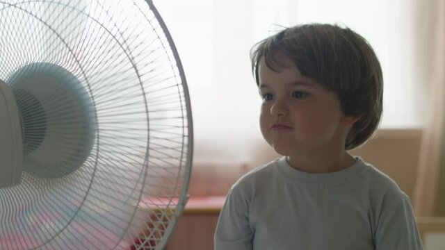 Boy Standing in Front of FBoy Standing in Front of Fan. Child Enjoying Cool Wind From Electric Fan at Home at Summer Vacation. Suffer From Heat High Temperature in Front of Ventilator Cooling Herself