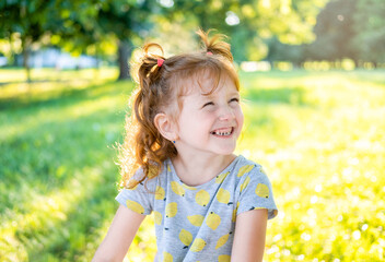 A beautiful little girl in the park in the sunset. Elementary age girl  smiling while looking at the side. Little toddler girl in a t-shirt in meadow at sunset with yellow background
