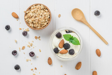 Yogurt with granola, blackberries and almonds on a white wooden table.