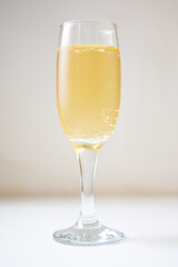 A glass of white sparkling wine. Champagne on the white table. Drink close-up. Gas bubbles in an alcoholic drink.