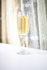 A glass of white sparkling wine. Champagne on the white table. Drink close-up. Gas bubbles in an alcoholic drink.