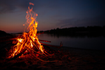 Bonfire on the river Bank at night. Red flames from burning branches and firewood near the...