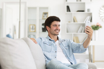 Relax millennial man using phone sitting on sofa at living room.