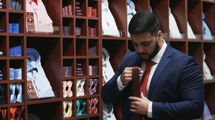 Bearded man dressed in elegant suit chooses his tie