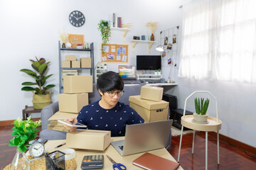 Asian man business owner working with laptop for checking packaging delivery e-commerce online market on purchase orders to customer
