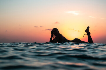 Portrait from the water of surfer girl with beautiful body on surfboard in the ocean at colourful...