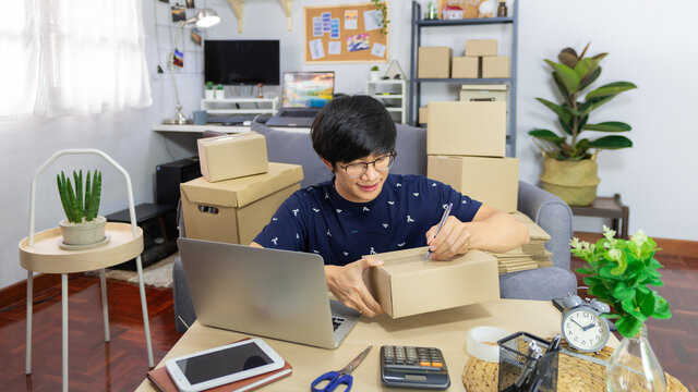 Asian man business owner working with laptop for checking packaging delivery e-commerce online market on purchase orders to customer
