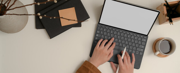 Hands typing keyboard tablet on white table with notebook, notepad, pencils and vase