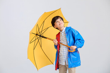 Cute little boy in raincoat and with umbrella on light background