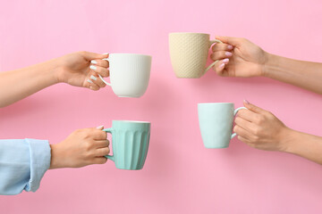 Hands with cups of hot coffee on color background