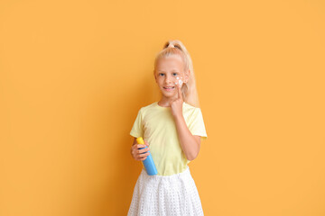 Little girl with sun protection cream on color background