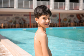 Little boy with sun protection cream on his body near swimming pool