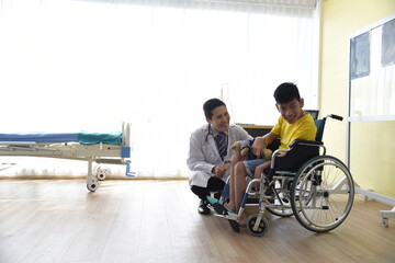 An Asian male Doctor taking care and look after Disabled boy Patient /cripple who can not help himself sitting on wheelchair in hospital/Disability