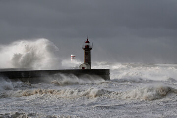 Fototapeta na wymiar Stormy waves over piers and lighthouse