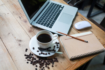 Coffee cups. Roasted coffee beans. Notebooks and pencils. The laptop is placed on a wooden table in the garden. Side angle