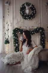 happy young woman with cup of coffee or tea near the fireplace at home bedroom