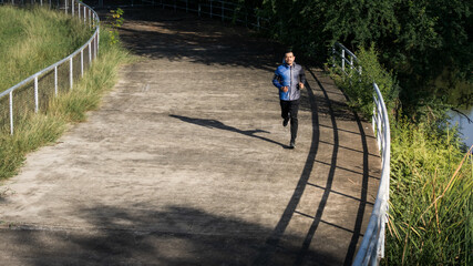 A man in sport hoodie jogging in the city park in the evening after stressful work. Runner jogging training and workout exercising power walking outdoors in forest city. Stock photo