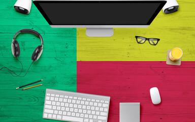 Benin flag background with headphone,computer keyboard and mouse on national office desk table.Top view with copy space.Flat Lay.