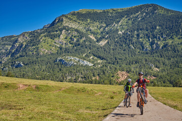 Fototapeta na wymiar two men on a mountain bike on a mountain road, one does a wheelie