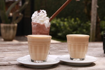 two cups of coffee and one cup of chocolate milkshakes on a wooden table.