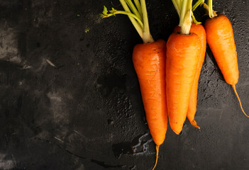Selective focus, ripe fresh carrots with a green stem on a black table, copyspace