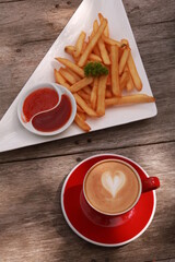 a cup of coffee and french fries on a wooden table.
