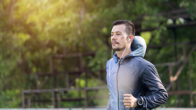A man in sport hoodie jogging in the city park in the evening after stressful work. Runner jogging training and workout exercising power walking outdoors in forest city. Stock photo