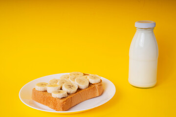 Top view - Grilled sliced bread topping with banana and bottle of milk over yellow background.