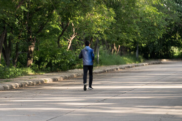 A man in sport hoodie jogging in the city park in the evening after stressful work. Runner jogging training and workout exercising power walking outdoors in forest city. Stock photo