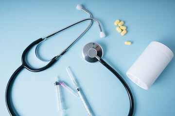 Doctor background - Stethoscope and medicine pills with syringe over blue background.