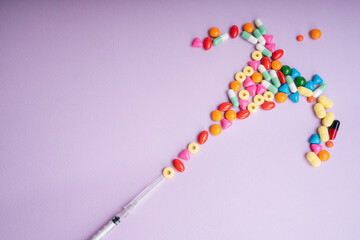 Syringe injection - Colourful medicine pills flowing out over pastel background.