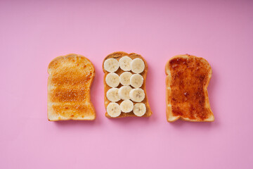 Top view - Grilled sliced bread topping with banan and jam over pink background.
