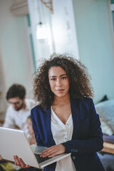 Good looking curly girl standing with open laptop in hands