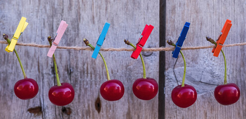 Cherry hanging on the scourge with colored clothespins on a gray wooden background