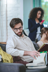 Bearded guy with glasses sitting on sofa with books, two girls