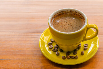 yellow cup coffee on wood background and coffee bean on the yellow plate or wooden table