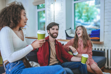 Cheerful guy and two girls on sides sitting on couch
