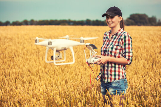 Agronomist Woman Walking On Field With Drone Flying Above Farmland At Sunset