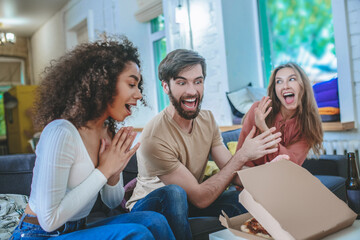Cheerful guy opening box with pizza and two enthusiastic girls