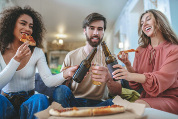 Three young friends with pizza and bottles touching one another