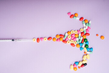 Syringe injection - Colourful medicine pills flowing out over pastel background.