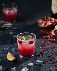 Close up shot of a Pomegranate Gin Fizz with a salt rim and lemon. On a dark background