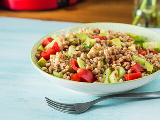 Fresh Italian farro spelt salad with tomatoes, avocado and cucumbers on wooden turquoise board. Easy recipe whole food meal