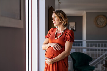 Pregnant woman standing near the window and thinking