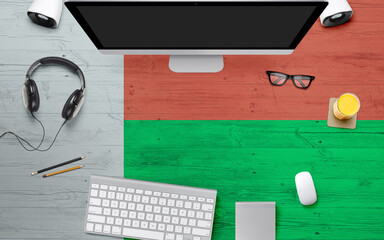 Madagascar flag background with headphone,computer keyboard and mouse on national office desk table.Top view with copy space.Flat Lay.