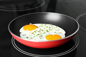 Chicken eggs with herbs in frying pan on stove, closeup