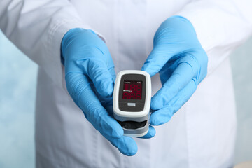 Doctor holding modern fingertip pulse oximeter, closeup