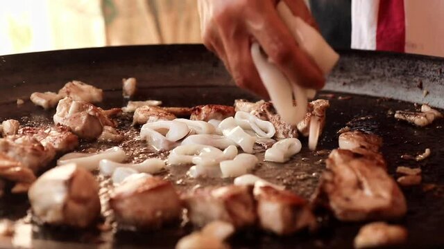 Closed frame about a cooker adding squids to the paella